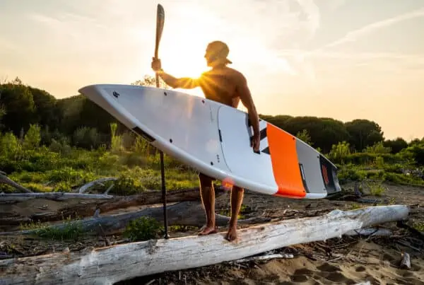 Supper draagt een SUP-board en peddel over het strand bij zonsondergang