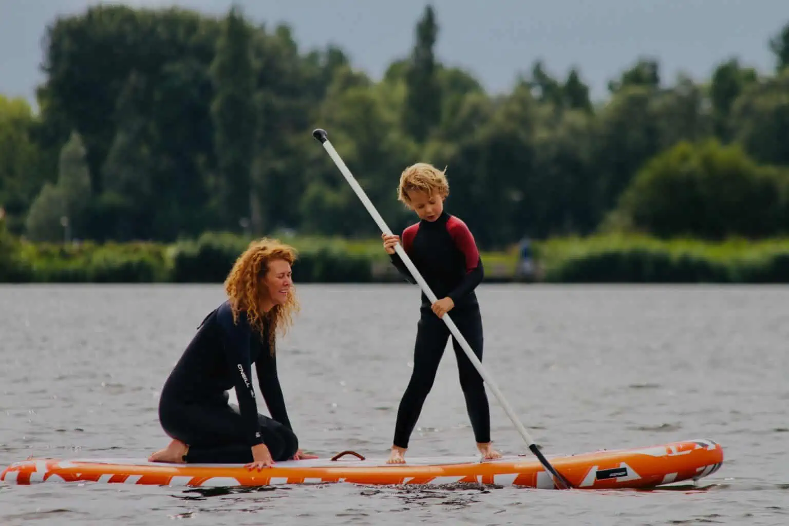 Volwassene en kind op een oranje SUP-board op het Valkenburgse Meer
