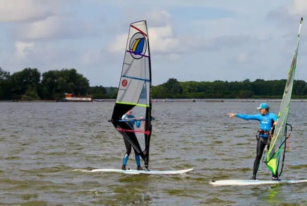 Cursist oefent windsurfen op het water bij GearFreak Surfschool