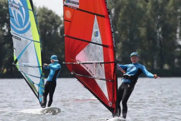 Twee windsurfers met rode zeilen bij GearFreak Surfschool