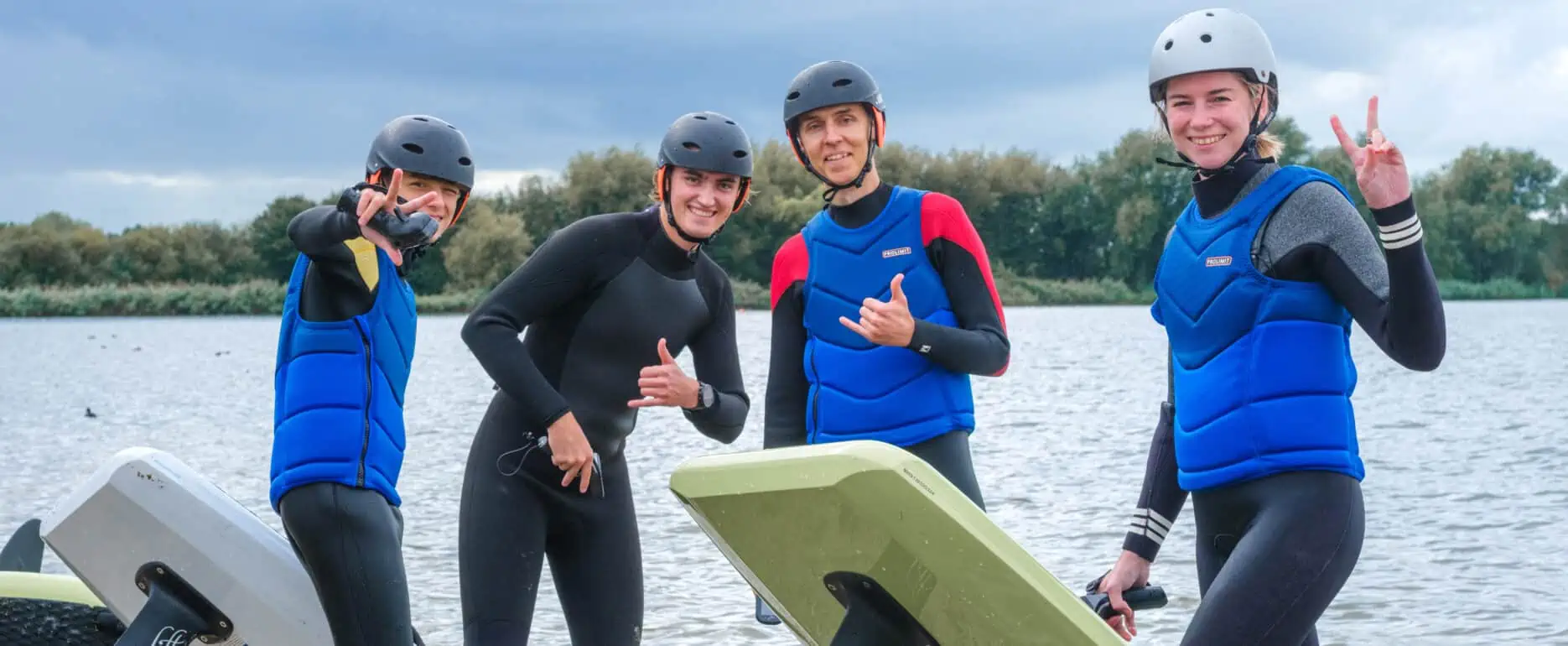 Vier cursisten met helm en impactvest poseren met twee Lift eFoils aan het Valkenburgse Meer